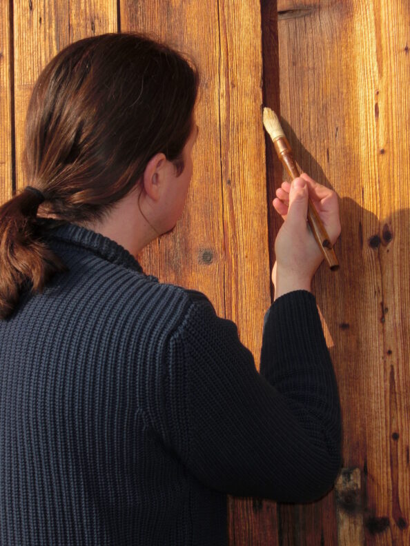 Holzschutz: Ein Mann streicht mit einem Pinsel ein Holztor.