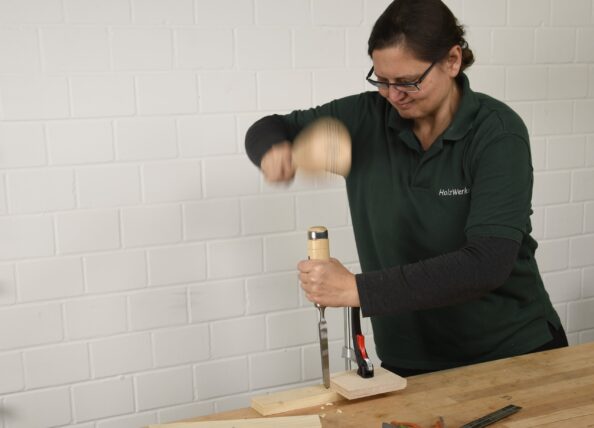 Eine Frau schlägt mit einem Klüpfel schwungvoll auf einen Stechbeitel.